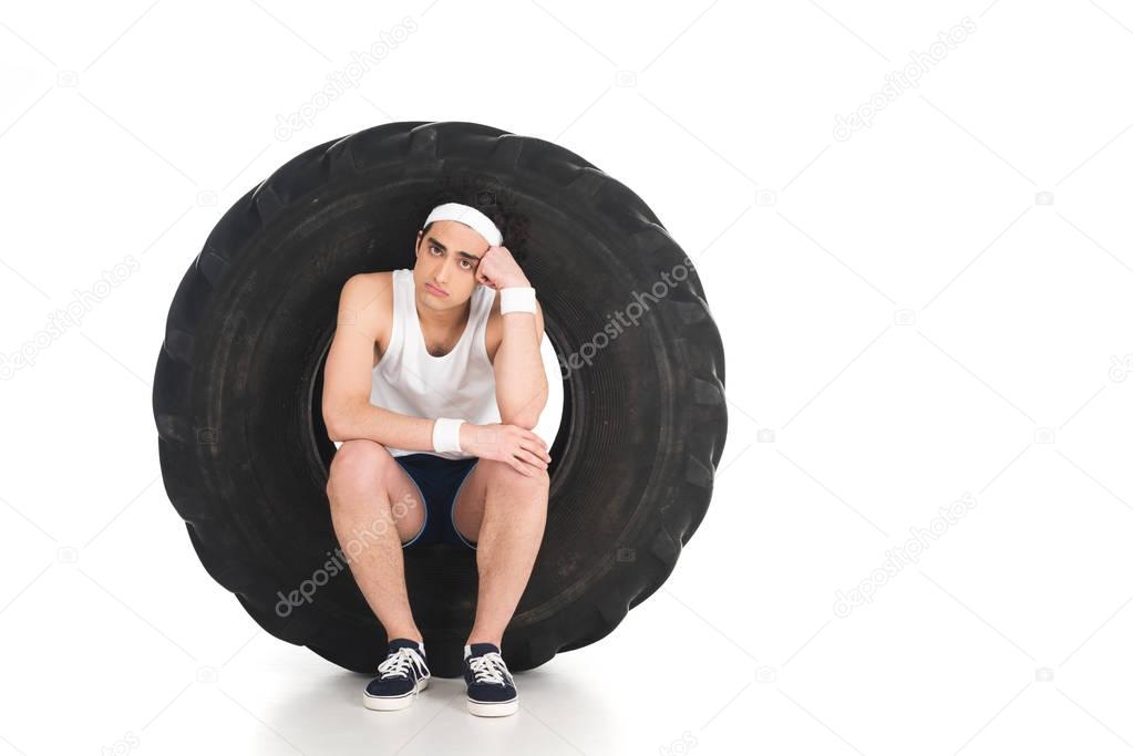 Young thin sportsman sitting inside wheel isolated on white