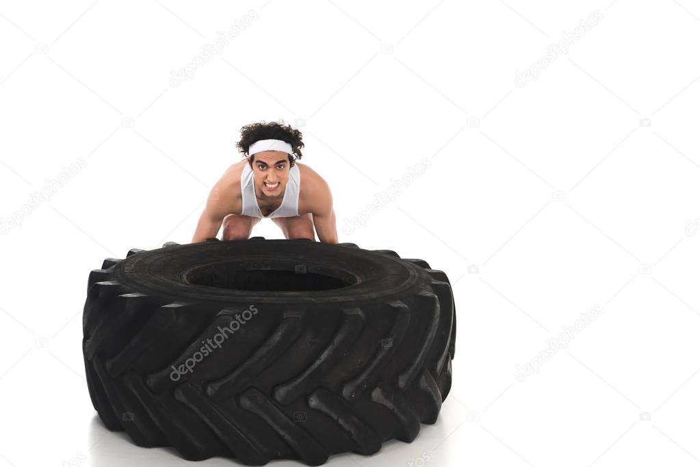 Young skinny sportsman raising tire of wheel isolated on white