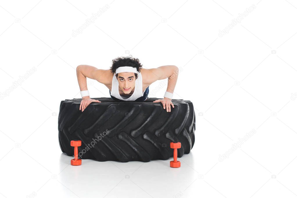 Young thin sportsman doing push ups on tire of wheel isolated on white