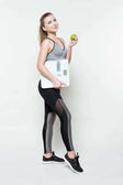 Mladá žena v sportovní top hospodářství apple a váhy izolované na bílém