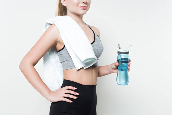 Close-up view of fit girl with towel on shoulder holding water bottle isolated on white
