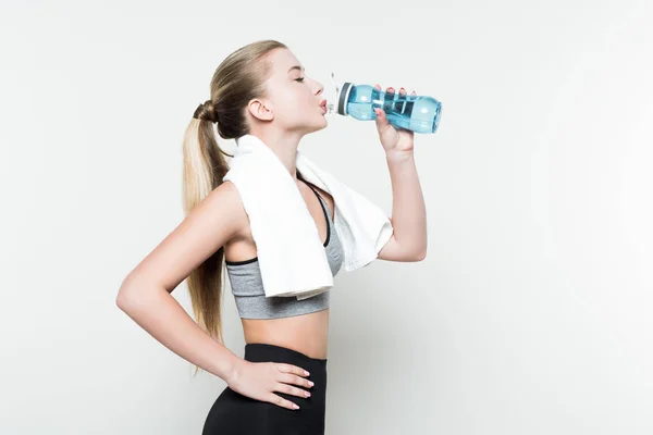 stock image Sportswoman with towel on shoulders drinking from water bottle isolated on white