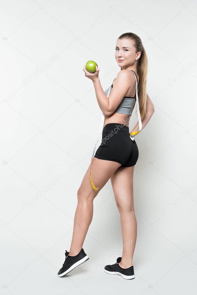 Fitness woman holding apple and measuring tape isolated on white