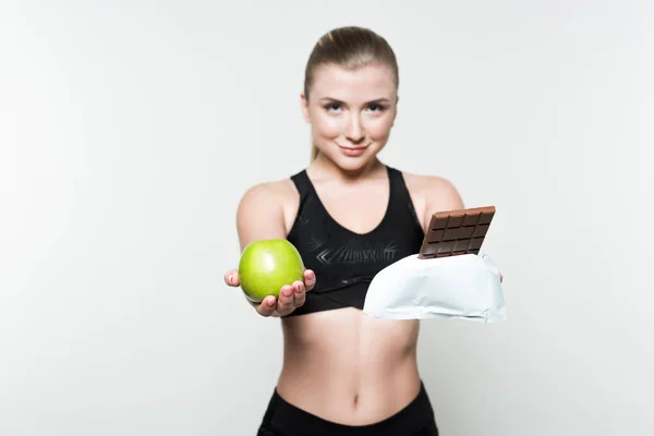 魅力的な女性はリンゴと白で隔離のチョコレート バーを保持しているスポーツ ウエア — ストック写真