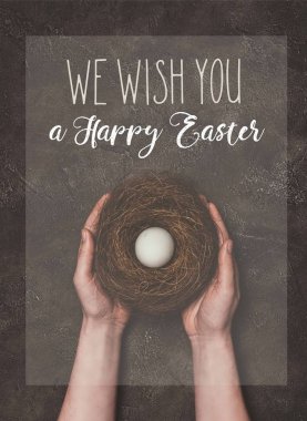cropped view of man holding nest with white egg, and We wish you a Happy Easter lettering clipart