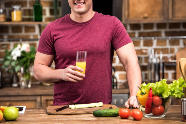 cropped shot of smiling young man holding glass of fresh orange juice at kitchen