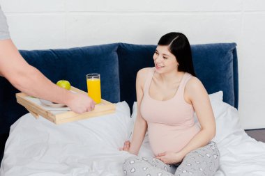 gülümseyen hamile kadın yatakta oturuyordu ise kahvaltı tepsisiyle tutan adamın kırpılmış atış