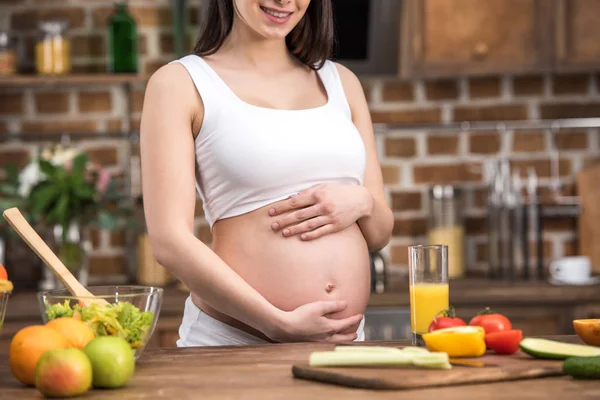 在准备健康早餐时微笑的年轻孕妇抚摸腹部的镜头 — 图库照片