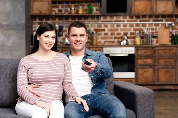 Happy Young Pregnant Couple Using Remote Controller Watching Together Home — Stock Photo, Image