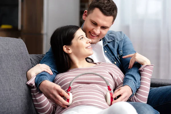 Feliz Joven Pareja Embarazada Usando Auriculares Para Vientre Casa —  Fotos de Stock