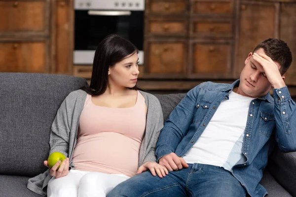 Young Pregnant Woman Holding Apple Looking Husband Sitting Sofa — Free Stock Photo