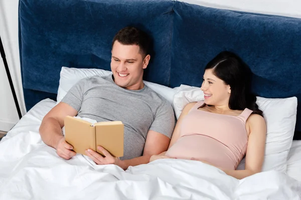 Happy Young Pregnant Woman Looking Man Reading Book Bed — Free Stock Photo