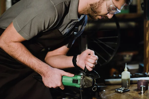 cropped shot of worker in protective goggles holding angle grinder in workshop