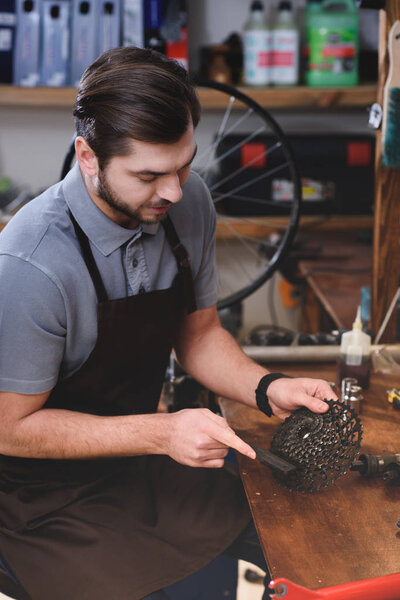 young man in apron working with bicycle chain in workshop