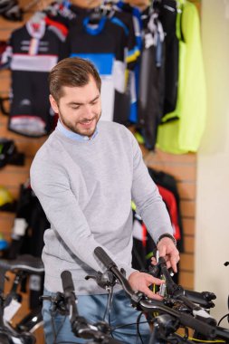 smiling young man looking at bikes in bicycle shop clipart