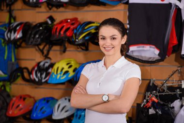 çapraz kolları ile ayakta ve bisiklet dükkanında çalışırken kameraya gülümseyen kendine güvenen genç kadın