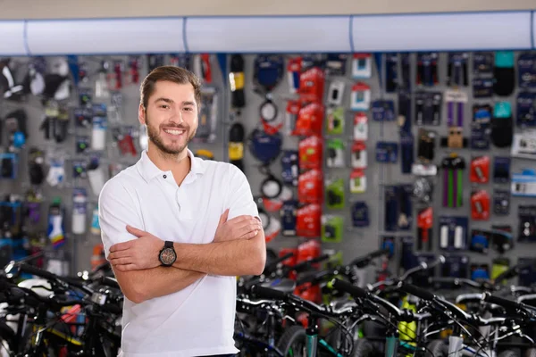 自信を持ってハンサムな若いマネージャー組んだ腕の側に立って 自転車店でカメラで笑顔 — ストック写真