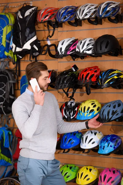 Smiling Young Man Talking Smartphone Choosing Bicycle Helmets Bike Shop — Stock Photo, Image