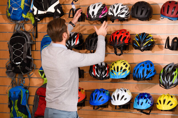 back view of young man choosing bicycle helmets in bike shop