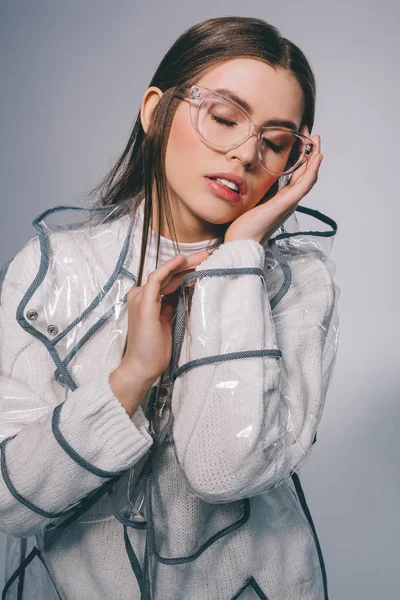 portrait of beautiful woman in stylish raincoat and eyeglasses posing on grey background