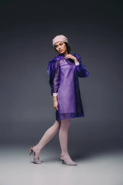 美丽的女人穿着时髦的紫色礼服和帽子摆在黑色背景 — 免费的图库照片