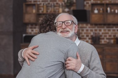 happy adult son and senior father hugging at home clipart