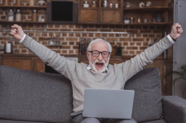 Happy grey hair man watching on laptop at home and celebrate win a bet with a gambling, soccer bet, sports gambling clipart