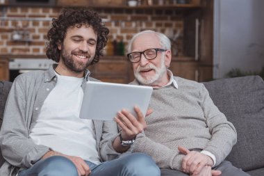 Yetişkin oğlum bir şey için üst düzey baba evde tablet üzerinde gösterilen gülümseyen