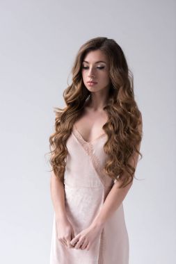 attractive curly model with long hair posing in pink dress, isolated on grey