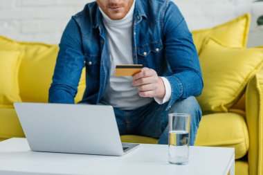Dizüstü bilgisayar kullanırken kredi kartı tutan genç adam