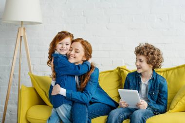 Anne ve kızı sarılmakla kanepede otururken oğlu holding tablet