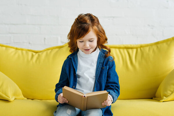 Enthusiastic little child reading book on sofa