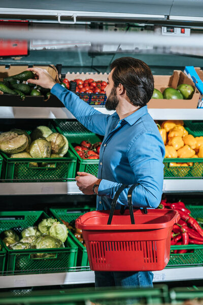 man with shopping basket choosing fresh vegetables in grocery shop