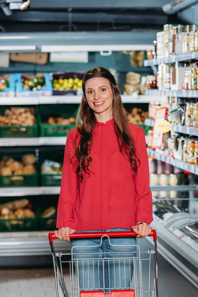 portrait of smiling woman with shopping trolley in supermarket