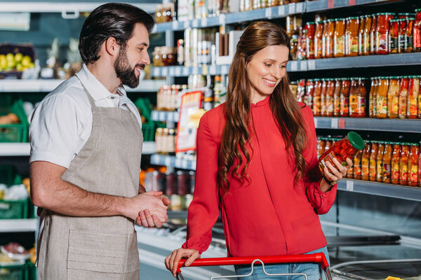 portrait of shop assistant in apron and female shopper in hypermarket
