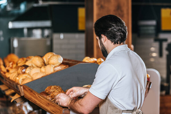 back view of male shop assistant arranging fresh bread in supermarket