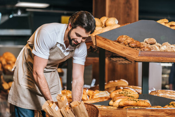 smiling male shop assistant arranging fresh pastry in supermarket