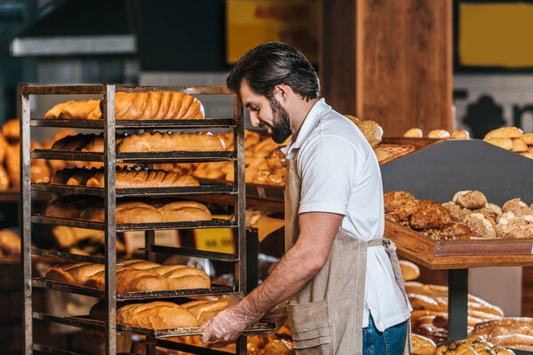 male shop assistant in apron arranging fresh pastry in supermarket
