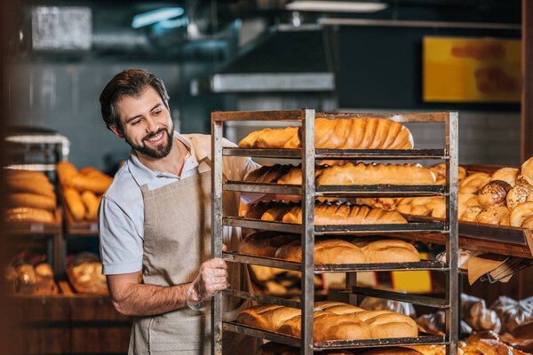 smiling male shop assistant arranging fresh pastry in supermarket