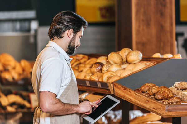 side view of shop assistant in apron using tablet with blank screen in supermarket