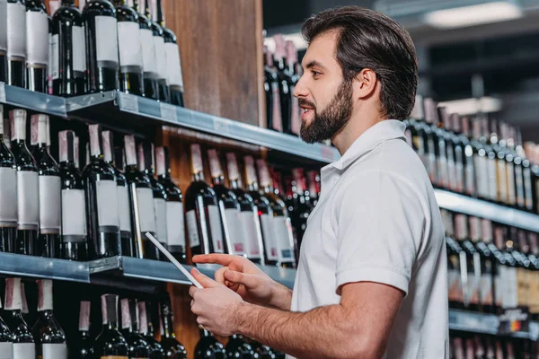 タブレットの大型スーパー マーケットのワインのボトルを見ていると店員の側面図 — ストック写真