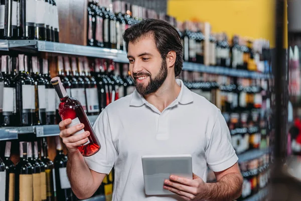 Portret Van Lachende Winkelbediende Met Tablet Kijken Fles Wijn Hypermarkt — Stockfoto