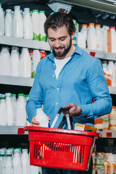 man putting bottle of milk into shopping basket in supermarket