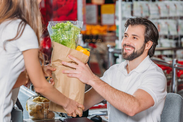 smiling shop assistant giving purchase to shopper in supermarket
