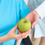 Cropped shot of doctor passing green apple to pregnant woman on wheelchair