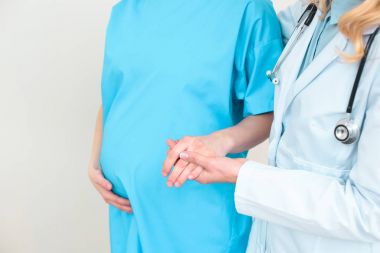 cropped shot of obstetrician gynecologist helping pregnant woman to walk and holding her hand clipart