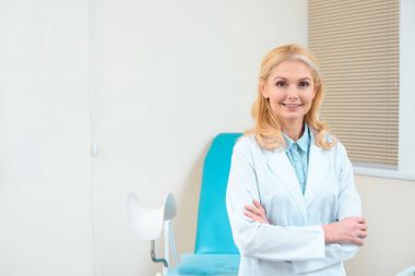 Olgun kadın jinekolog kadın hastalıkları sandalye önünde çapraz kolları olan