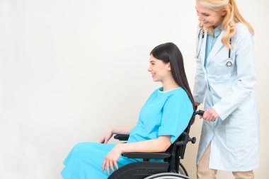 side view of obstetrician gynecologist riding pregnant woman on wheelchair at maternity hospital