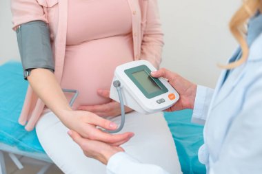 cropped shot of obstetrician gynecologist measuring blood pressure of pregnant woman at clinic clipart