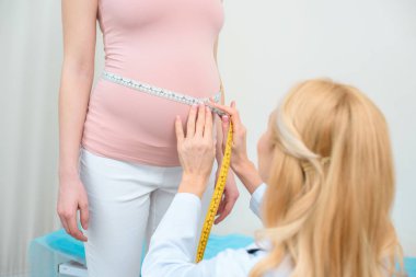 female obstetrician gynecologist measuring belly size of pregnant woman with measuring tape clipart